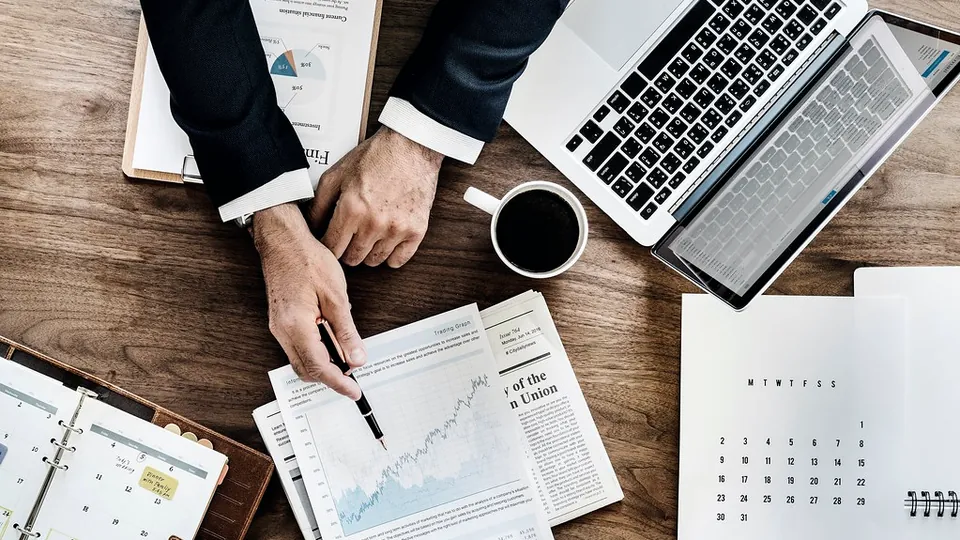 Hands reviewing printed financial statements and charts next to a laptop
