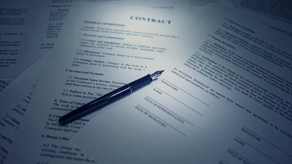 A fountain pen resting on printed contract pages under a desk lamp