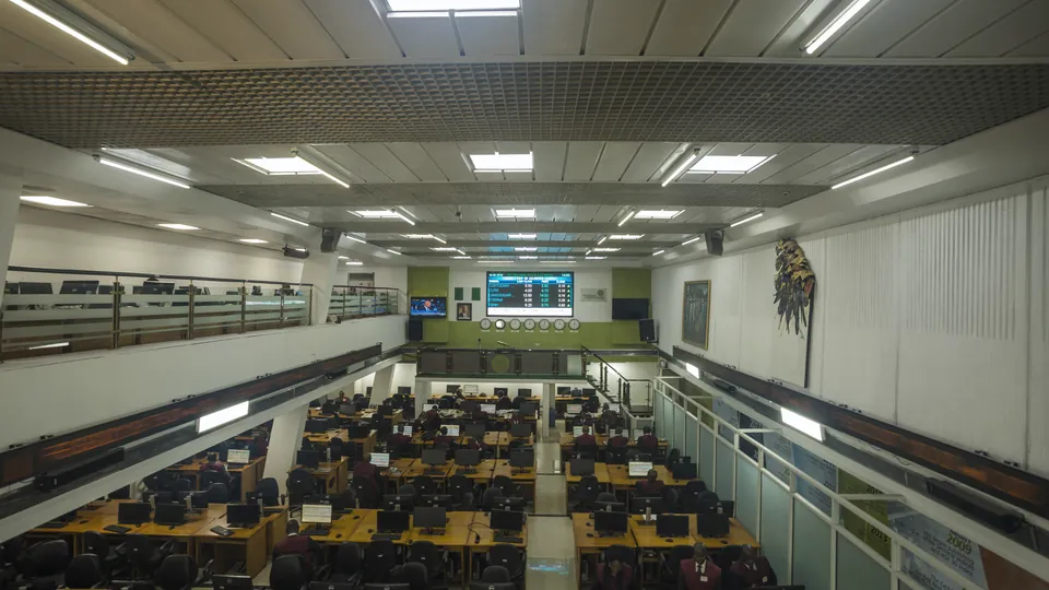 A stock exchange trading room with rows of trader desks and screens under a quote board